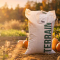 Sac de TERRAIN AUTOMNE 7 kg posé dans un jardin entouré de citrouilles, lumière du coucher de soleil